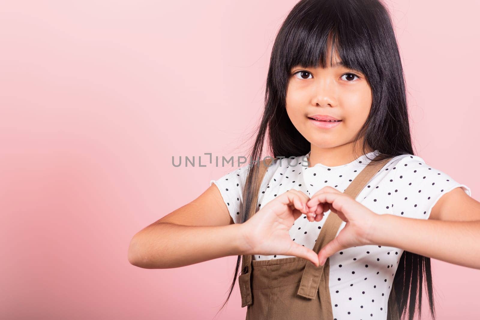 Asian little kid 10 years old showing heart sign at studio shot isolated on pink background, Happy child girl making heart shape gesture with hands, Cheerful kid, Valentine day