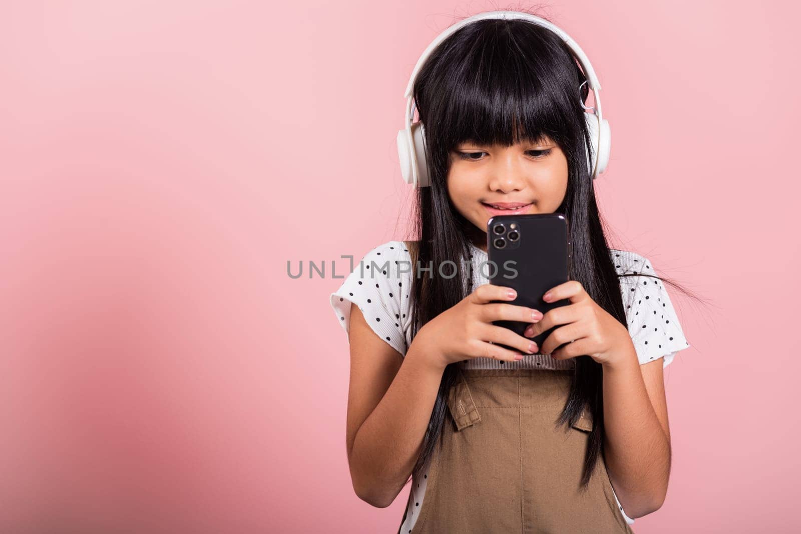 Asian kid 10 years enjoying listening music from mobile phone wear wireless headset at studio shot isolated on pink background, Happy child girl lifestyle use smartphone listen music with headphones