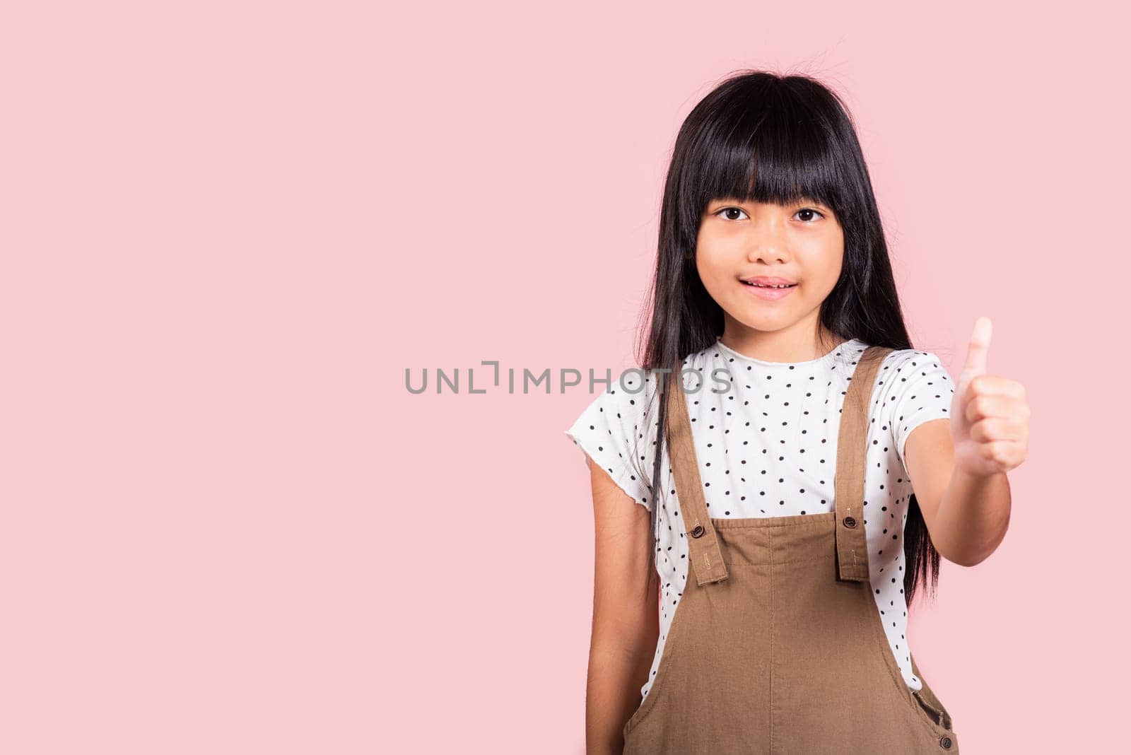 Asian little kid 10 years old showing thumbs up at studio shot isolated on pink background, Portrait of happy child girl positive smiling show finger for good gesture