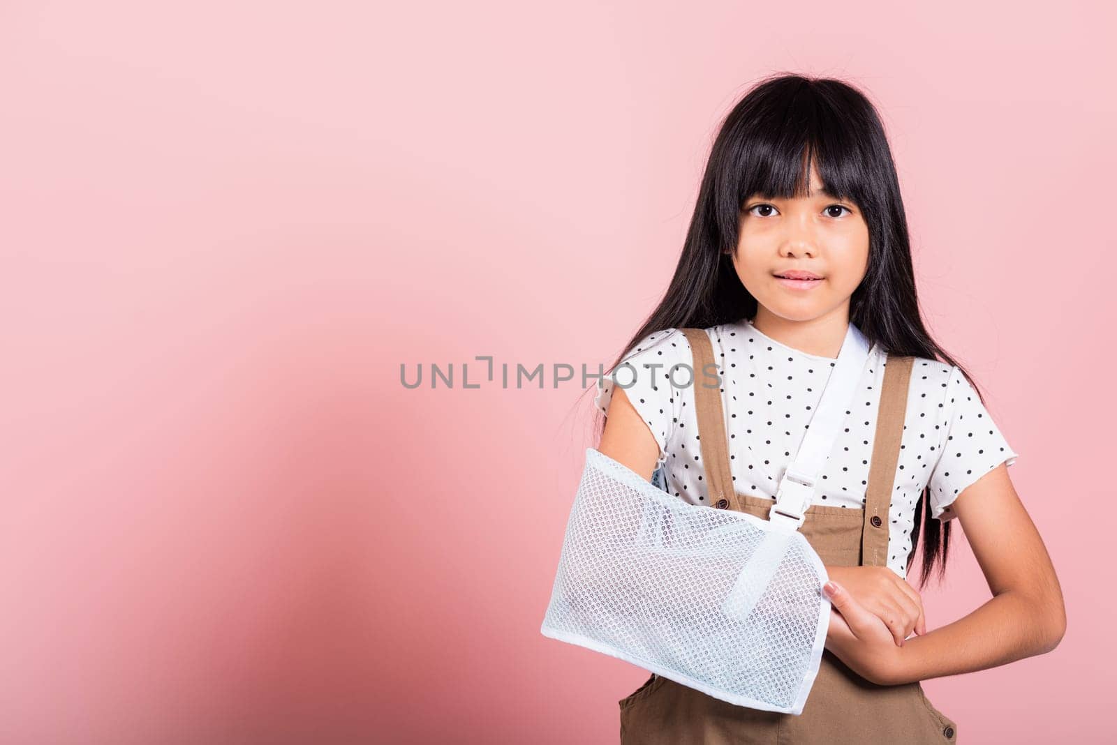 Arm broken. Asian little kid 10 years old hand bone broken from accident with arm splint at studio shot isolated on pink background, Happy child girl accident insurance and extreme sports speed