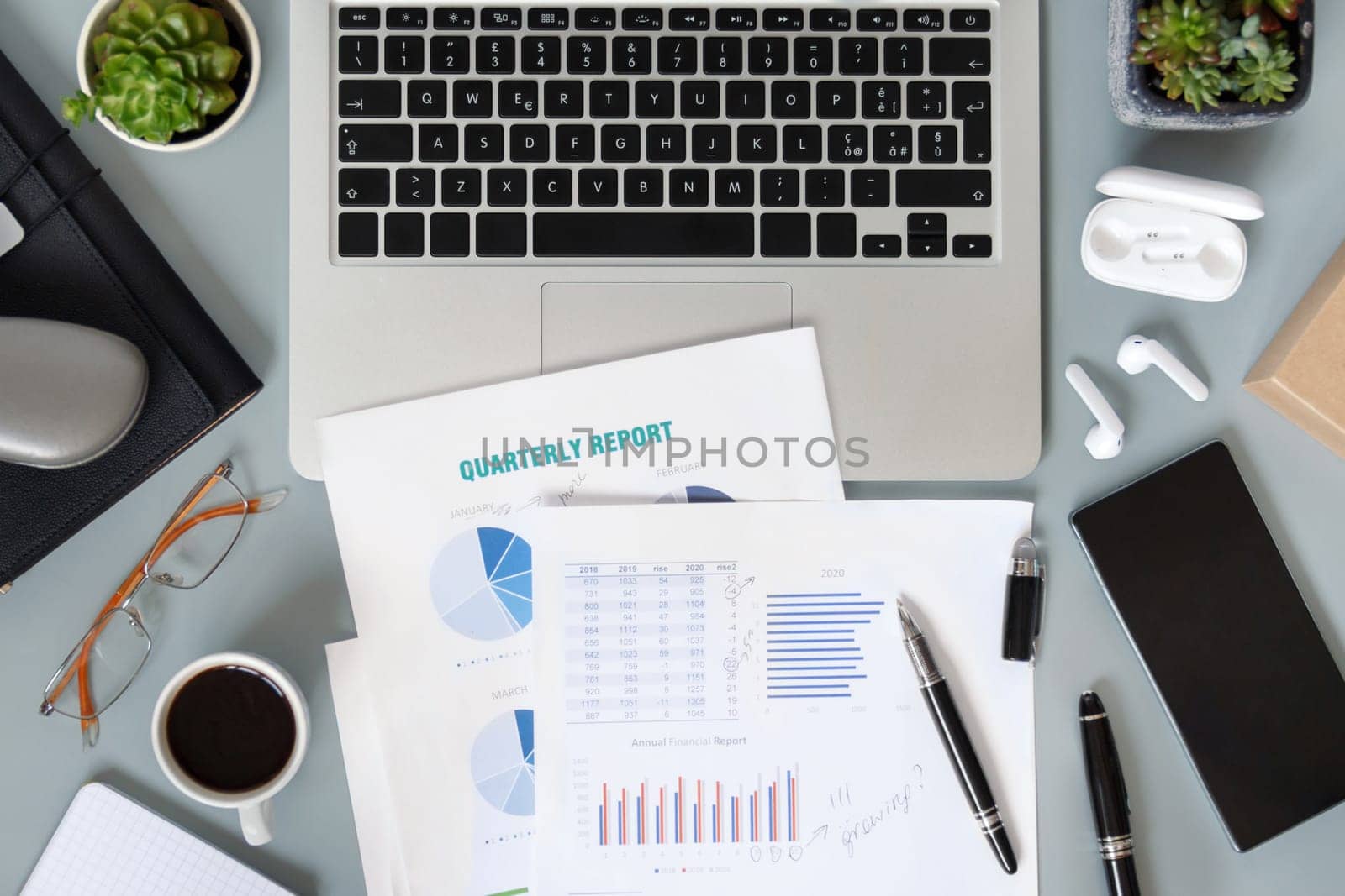 Modern office desktop with laptop, succulent plants, documents and gadgets top view. Working on quarterly reports with coffee cup. Smark working at home