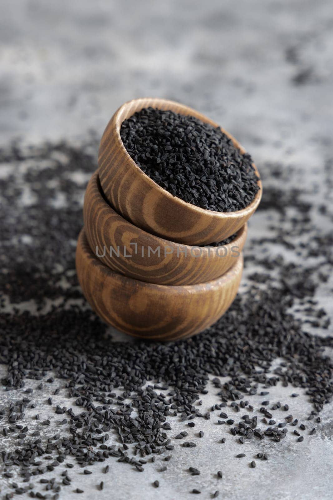 Indian spice Black cumin (nigella sativa or kalonji) seeds in wooden bowls on grey table close up. Traditional medicine, healthy and vegetarian food concept.