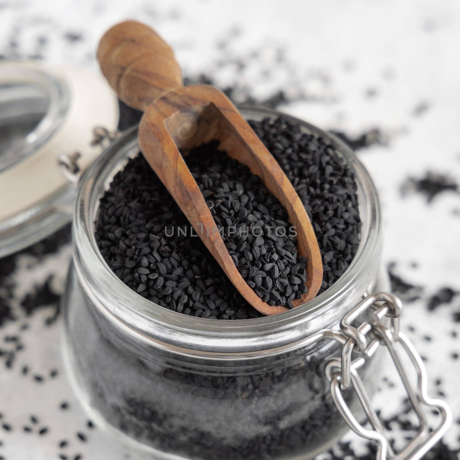 Indian spice Black cumin (nigella sativa or kalonji) seeds glass jar with a wooden scoop, close up. Traditional asian medicine, healthy and vegetarian food concept