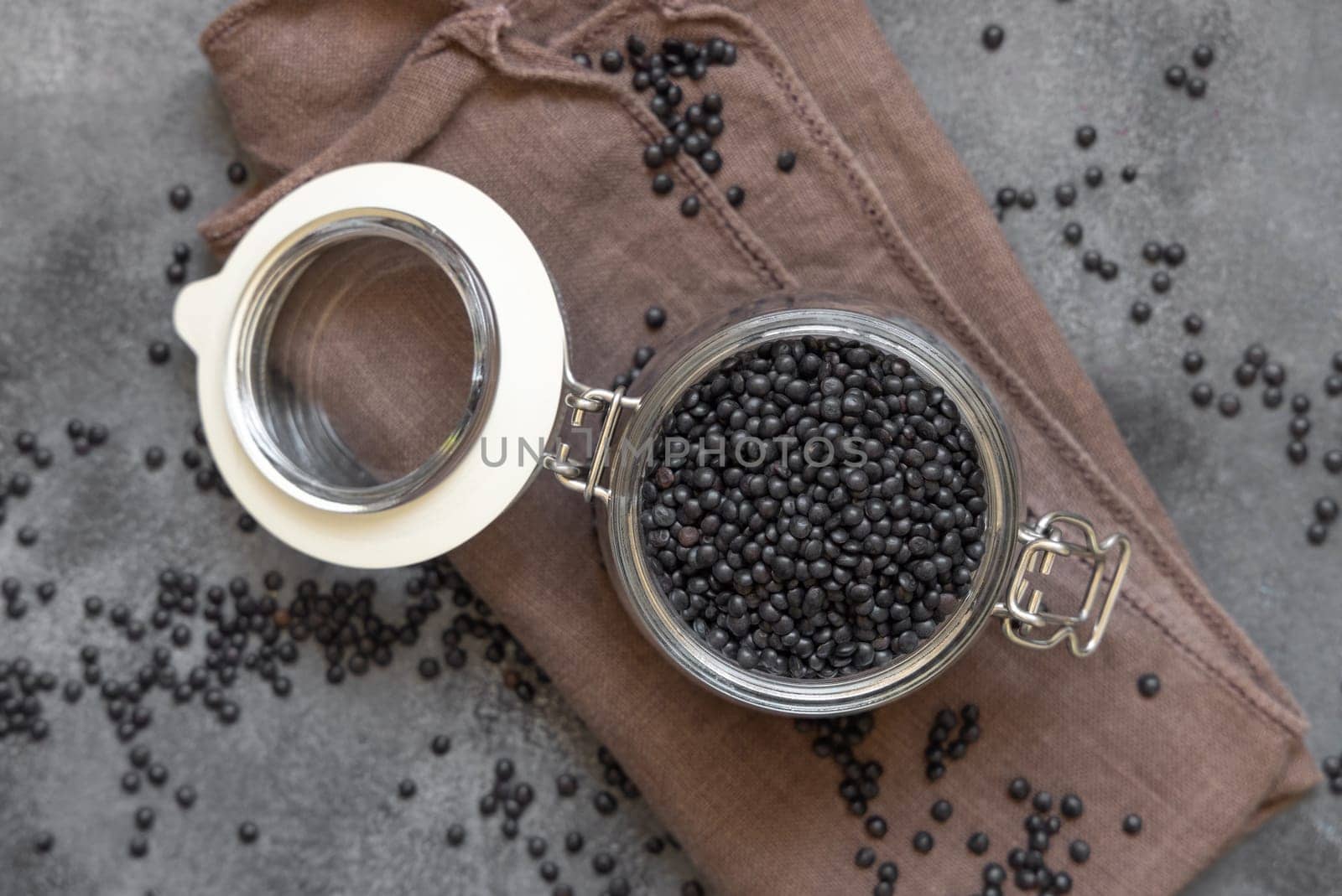 Glass jar of dry black lentils beans on grey table top view. Healthy eating, protein source for vegan and vegetarian diet. Traditional Asian and North African cuisines ingredient