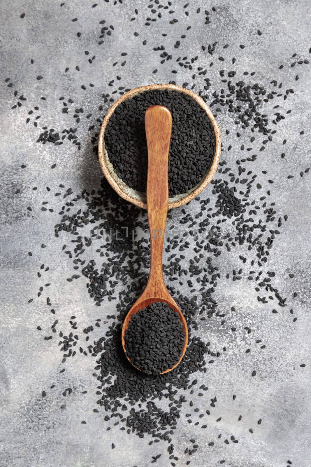 Bowl of Indian spice Black cumin (nigella sativa or kalonji) seeds on grey table with a wooden spoon, top view. Traditional asian medicine, healthy and vegetarian food concept