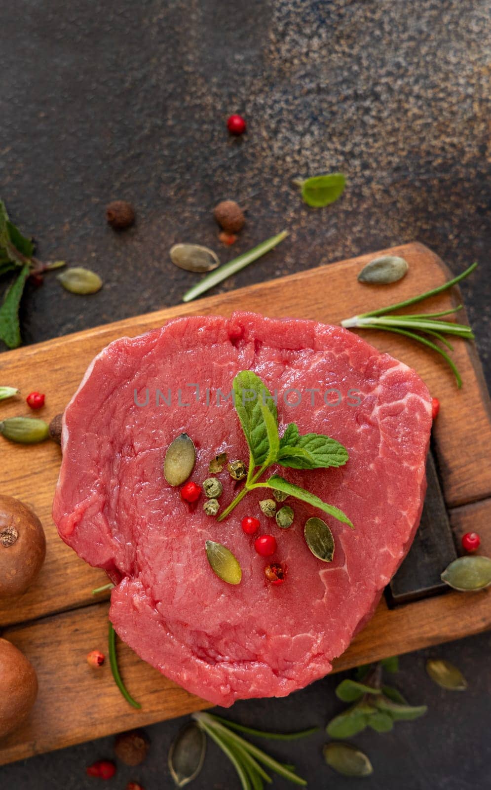 Raw beef fillet steak on wooden board on dark table top view. Portioned filet mignon with spices and herbs. Concept of summer food