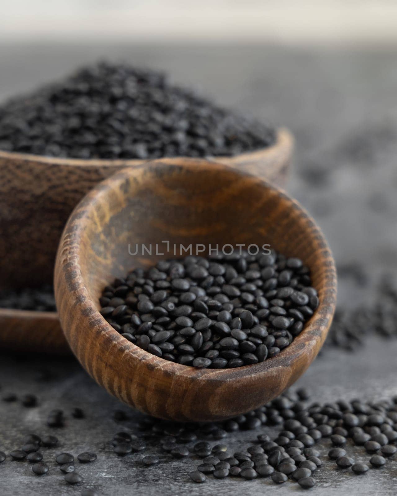 Wooden bowls of black beluga lentils beans on grey table close up. Healthy eating, protein source for vegan and vegetarian diet. Traditional Asian and North African cuisines ingredient