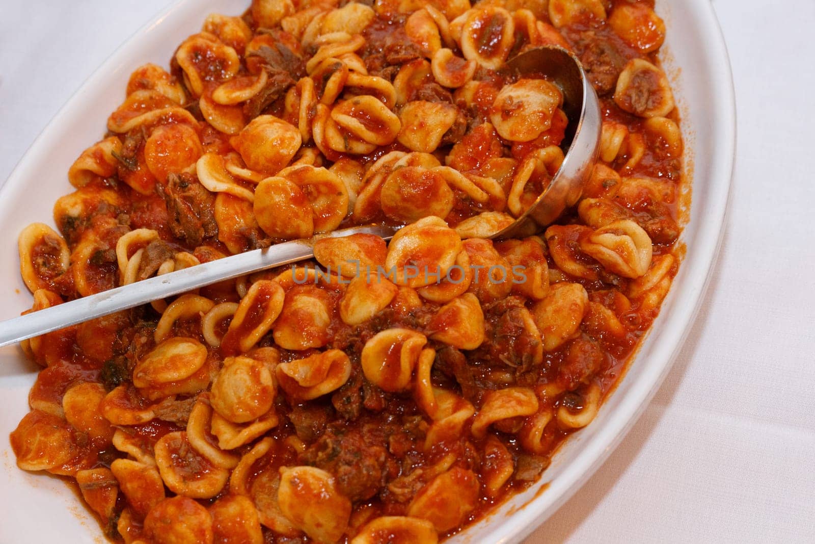 South italian pasta orecchiette with tomato sauce and minced meat ragu close up on a white table