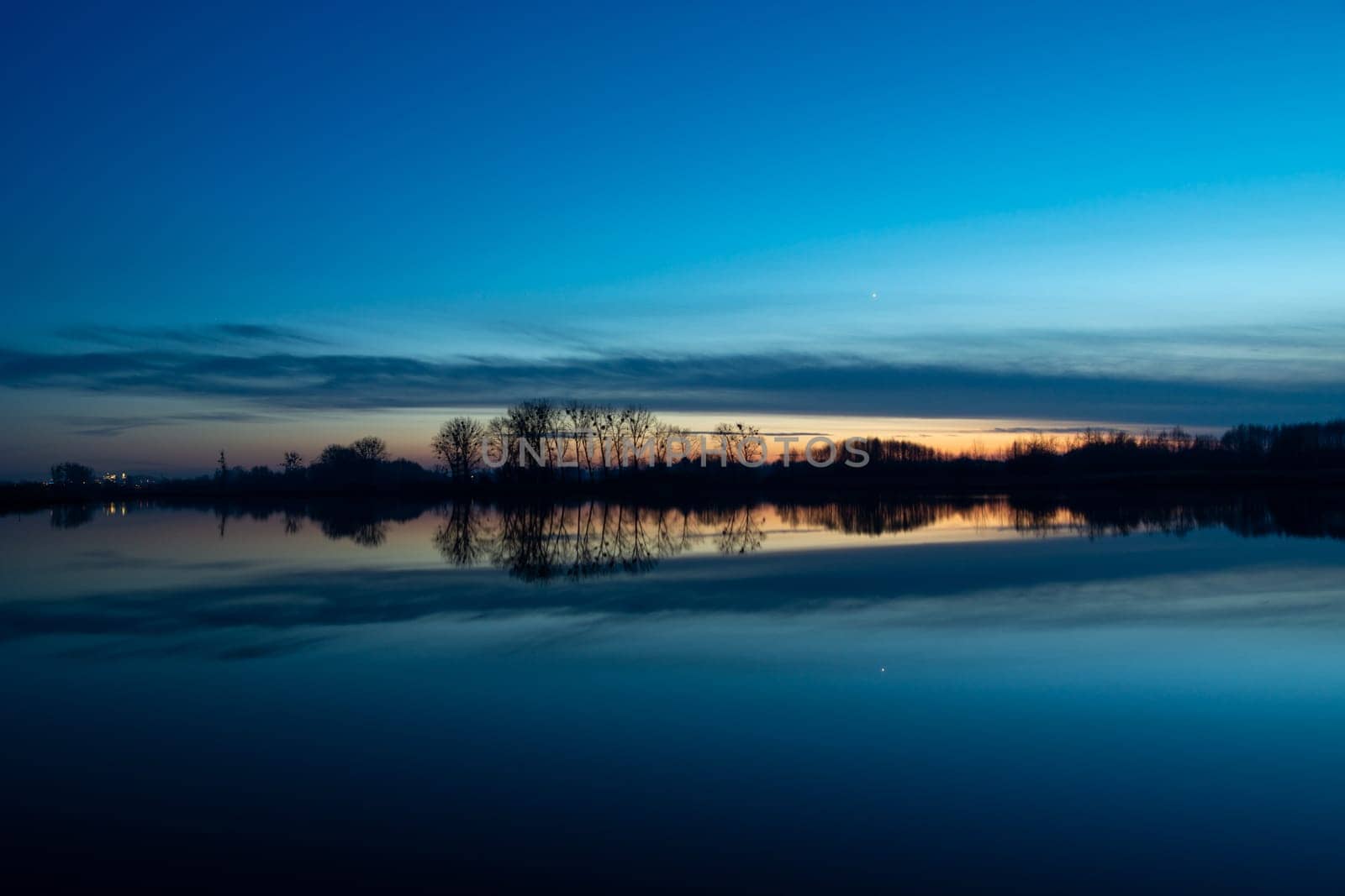 Reflection of trees and clouds in the lake water, sunset view