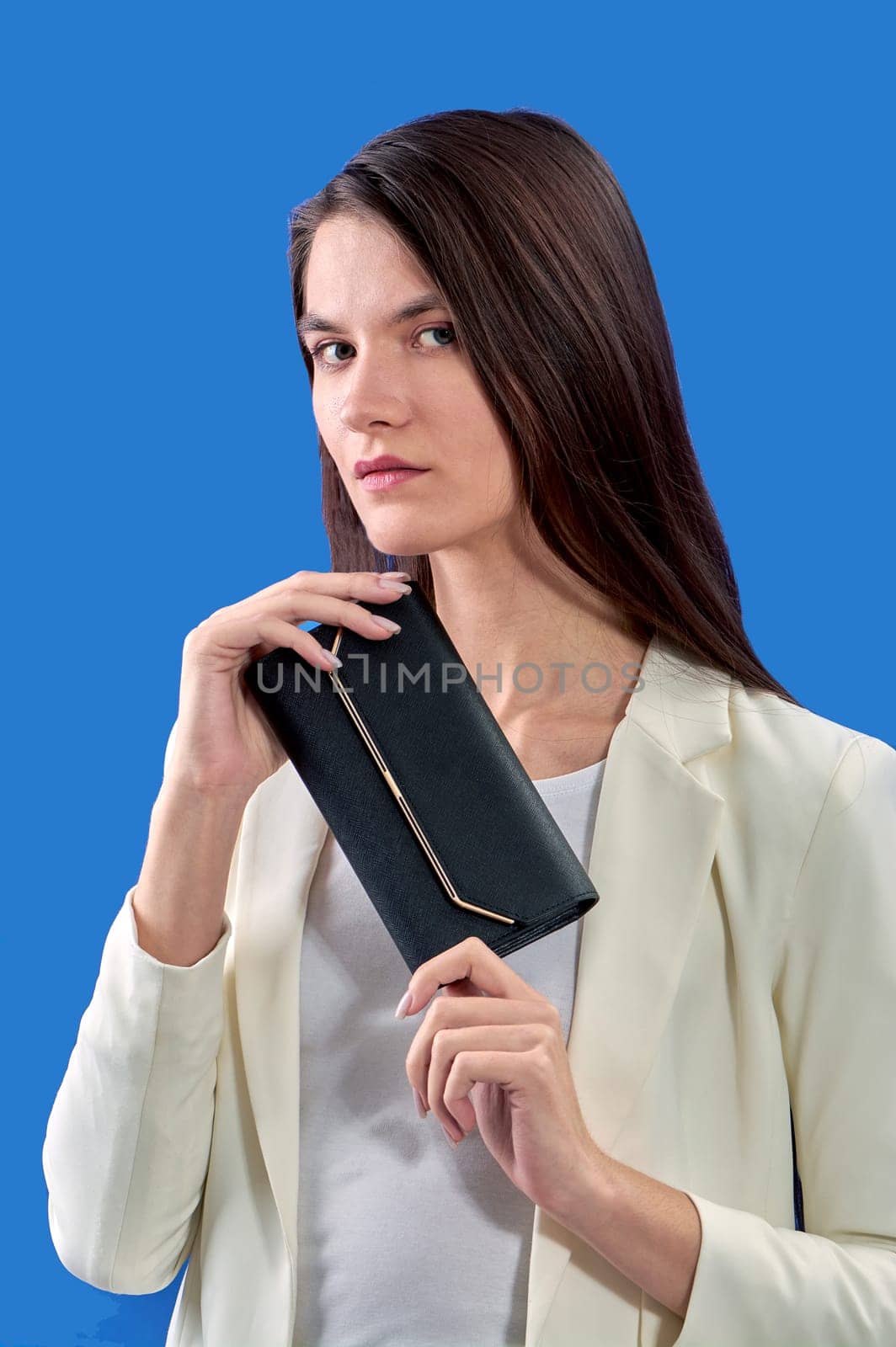 A beautiful young woman is holding a black handbag on a blue background. High quality photo