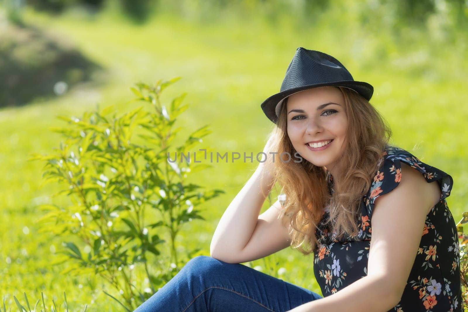 Portrait of attractive  young woman in black straw hat is sitting  outdoors in summer day. Horizontally.