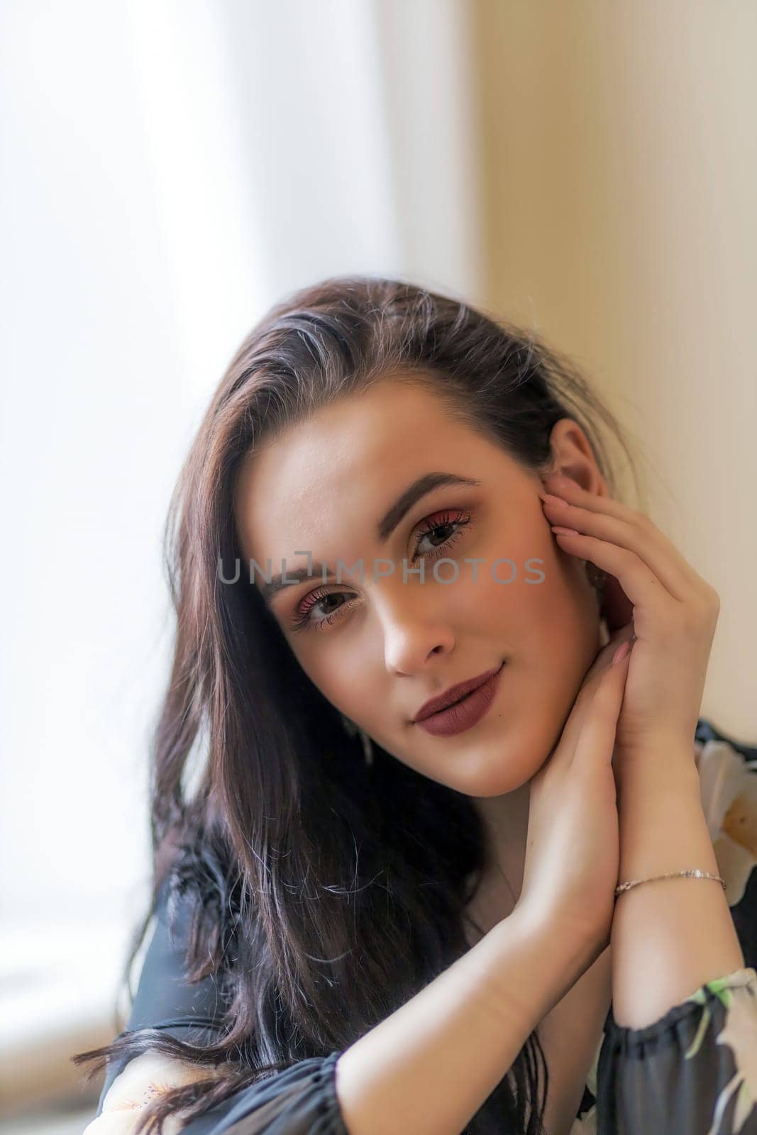 Portrait of attractive dark haired girl posing with hands on chin. Vertically.