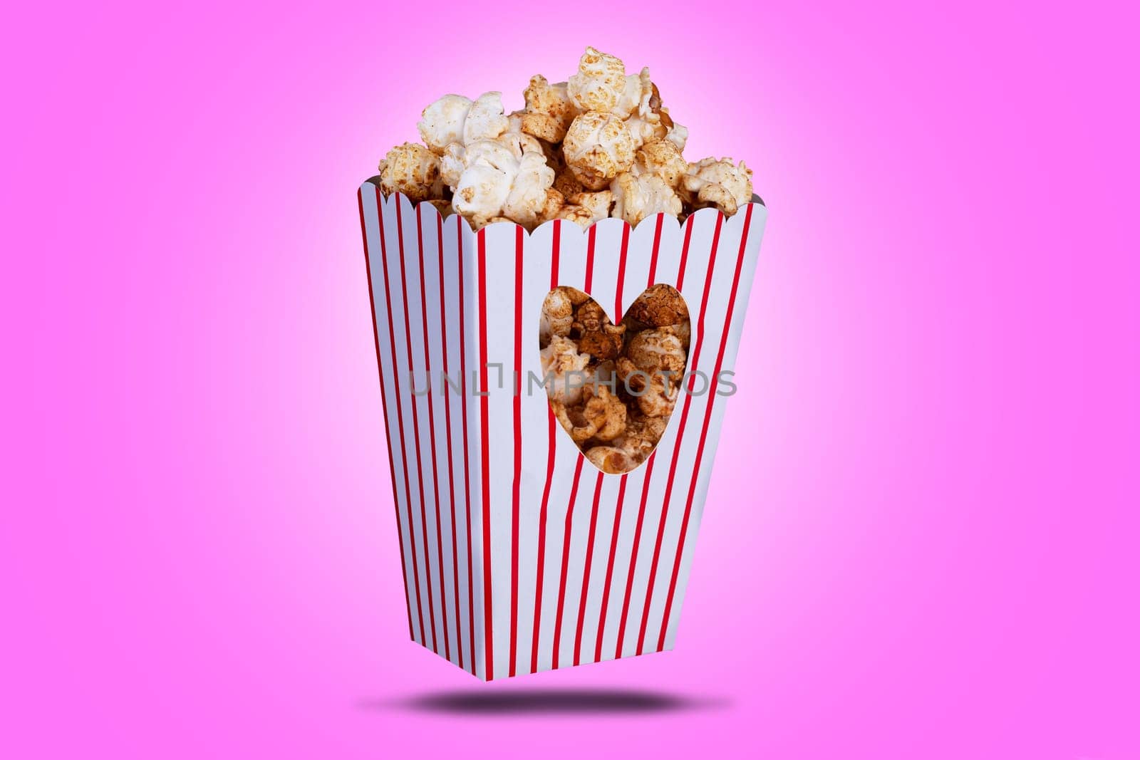 Popcorn in a box with a love heart cutout. Red striped packaging with snack food and a pink background.