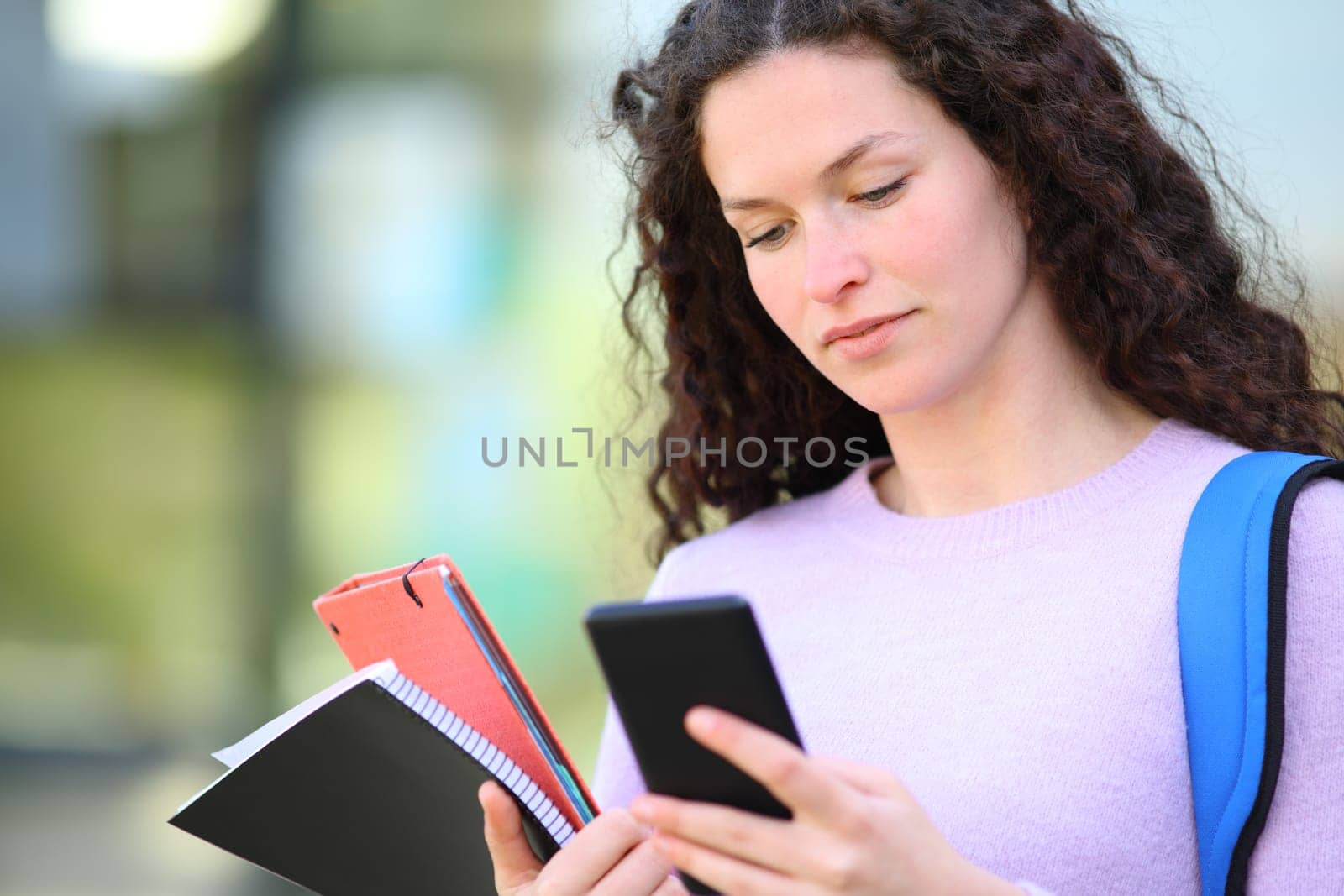 Serious student reading phone content in a campus