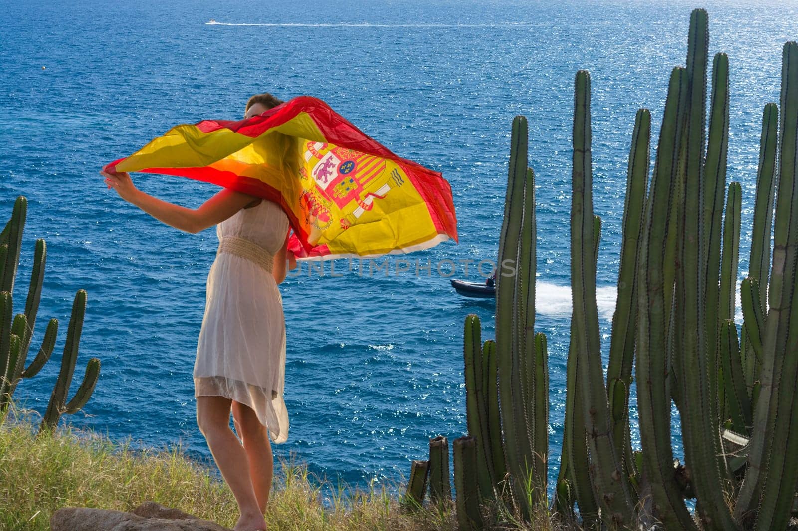 Young woman with Spain flag on a rock in the background the blue sea