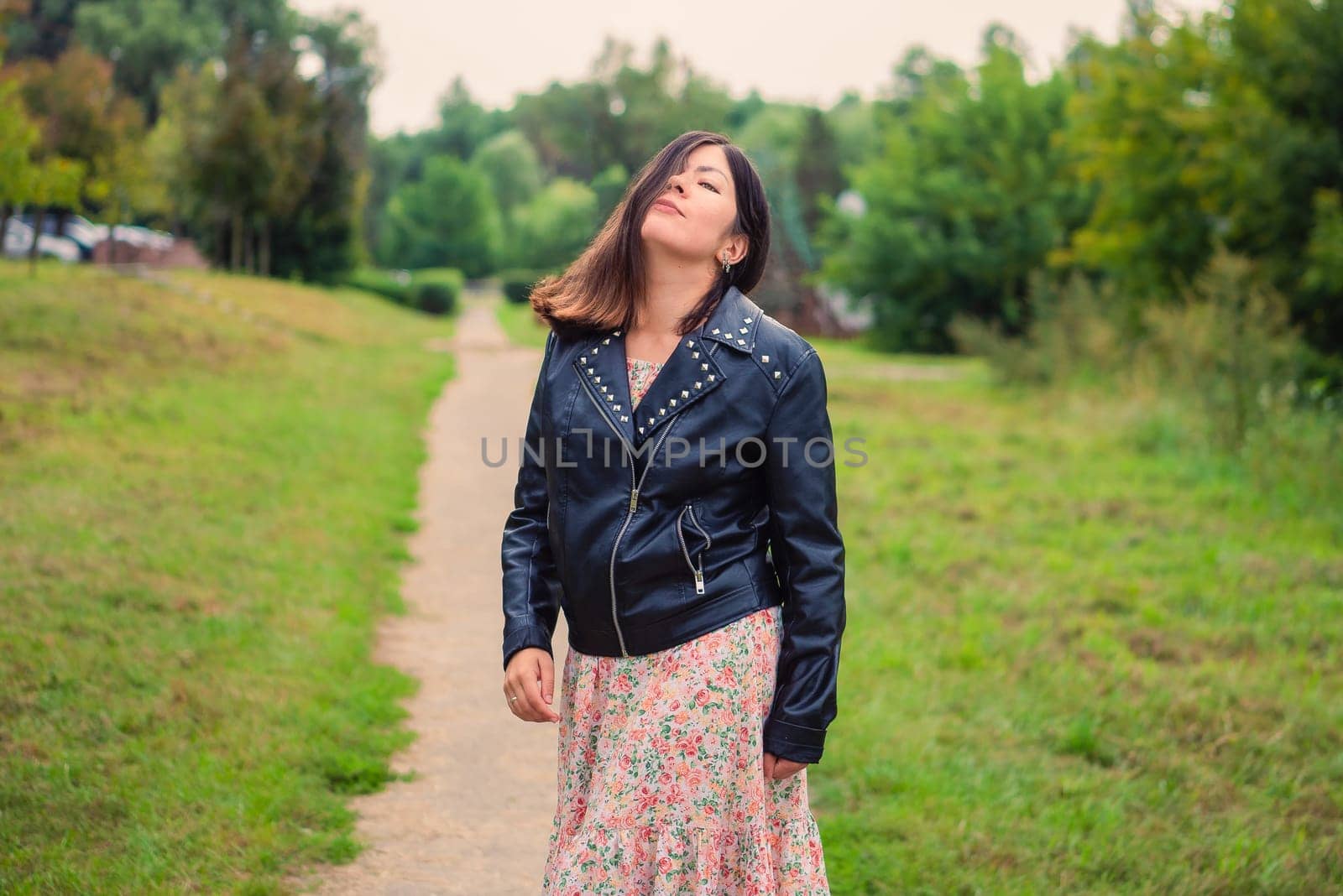 a beautiful young woman stands on a path in the park, covering half her face with her hair
