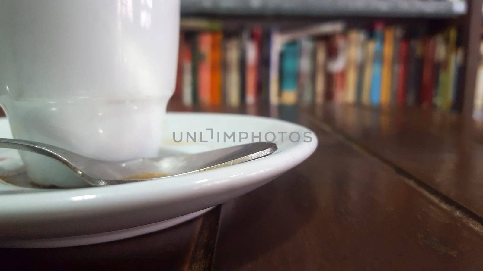 Little coffee cup over wooden table with book shelves background. Selective focus
