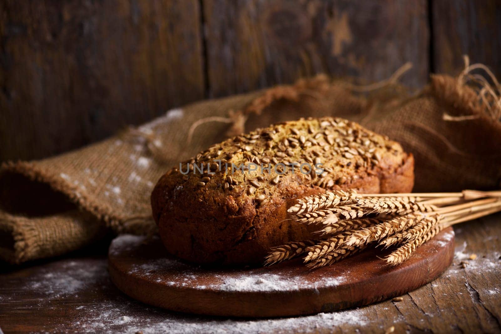 Homemade bread loaf and wheat ears on rustic wooden background