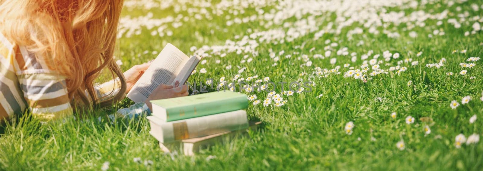 Young woman lying on the field and reading some books. Concept of hobby, relaxing and studying.