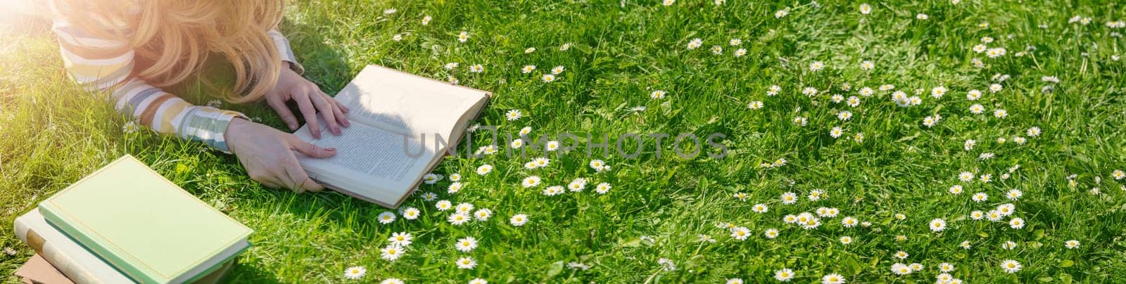 Young woman lying on the field and reading some books. Concept of hobby, relaxing and studying.