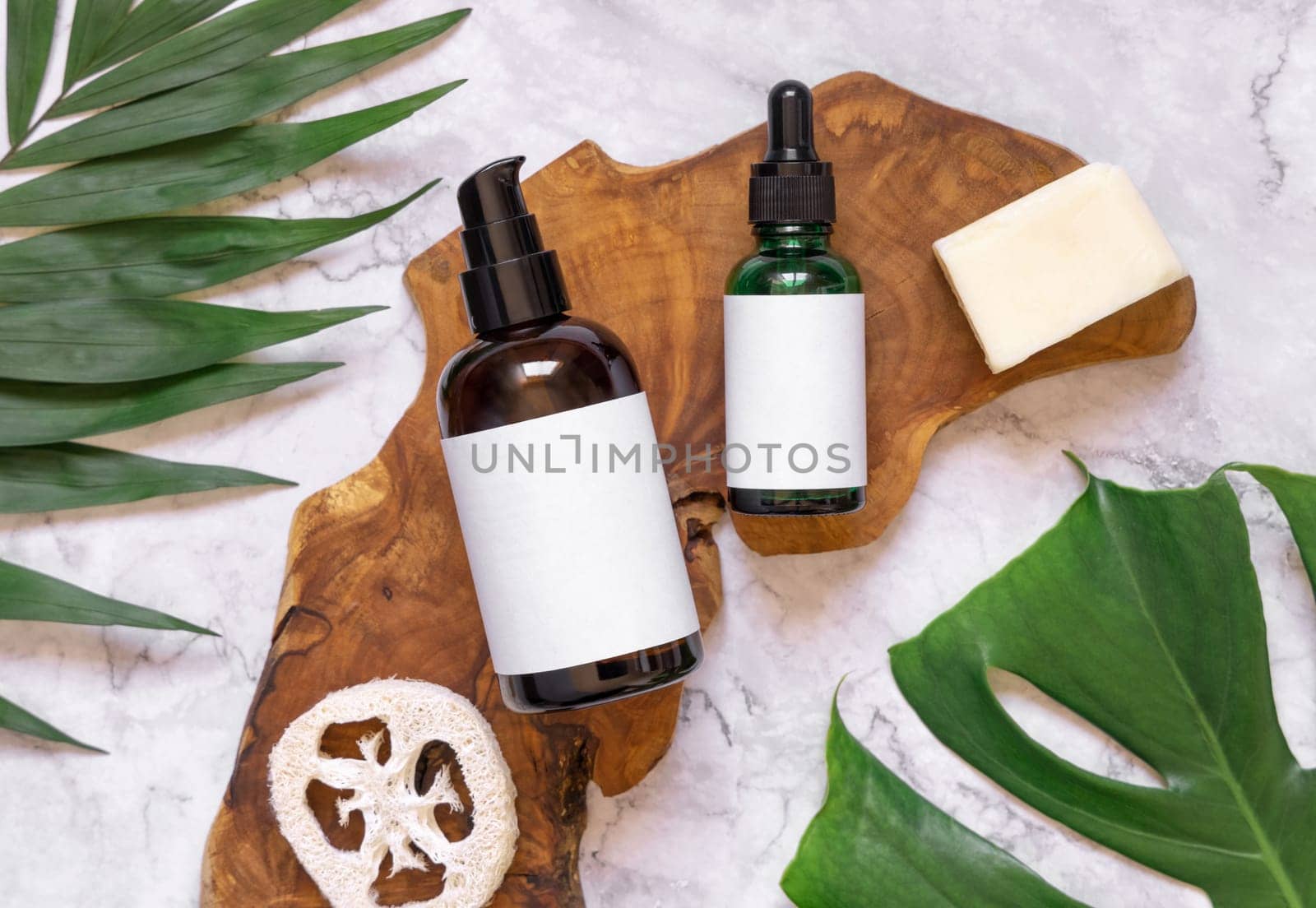 Natural cosmetics in glass bottles on a wooden board near monstera and palm leaves, flat lay, copy space. Brand packaging mockup. Organic beauty products for hair and skin care, Top view