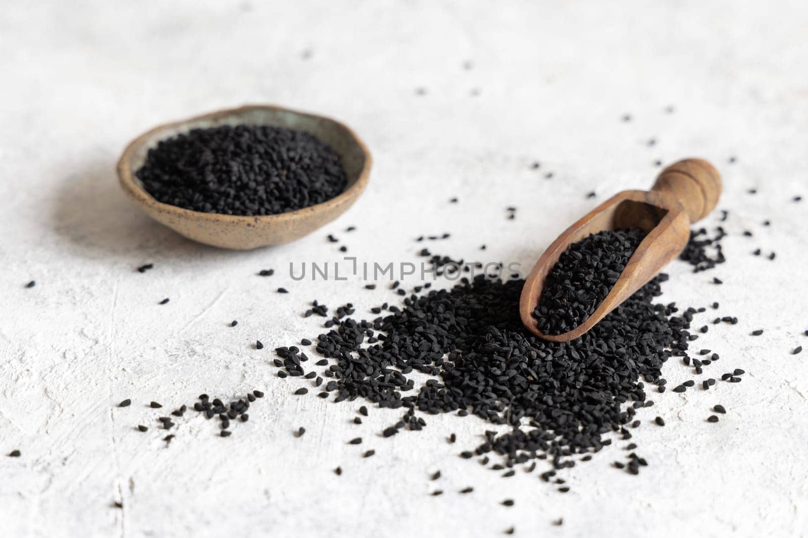 Scoop of Indian spice Black cumin (nigella sativa or kalonji) seeds on white table close up with copy space. Traditional medicine, healthy and vegetarian food concept.