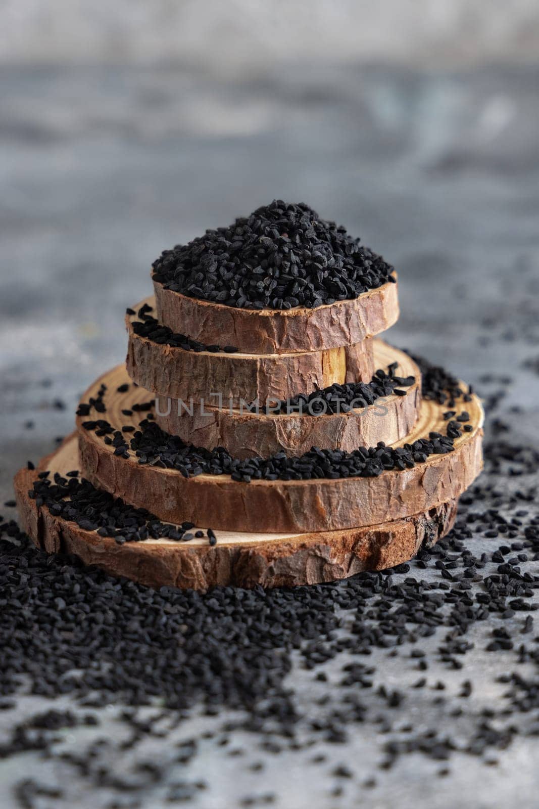 Indian spice Black cumin (nigella sativa or kalonji) seeds on grey table with a wooden spoon, close up with copy space. Traditional asian medicine, healthy and vegetarian food concept