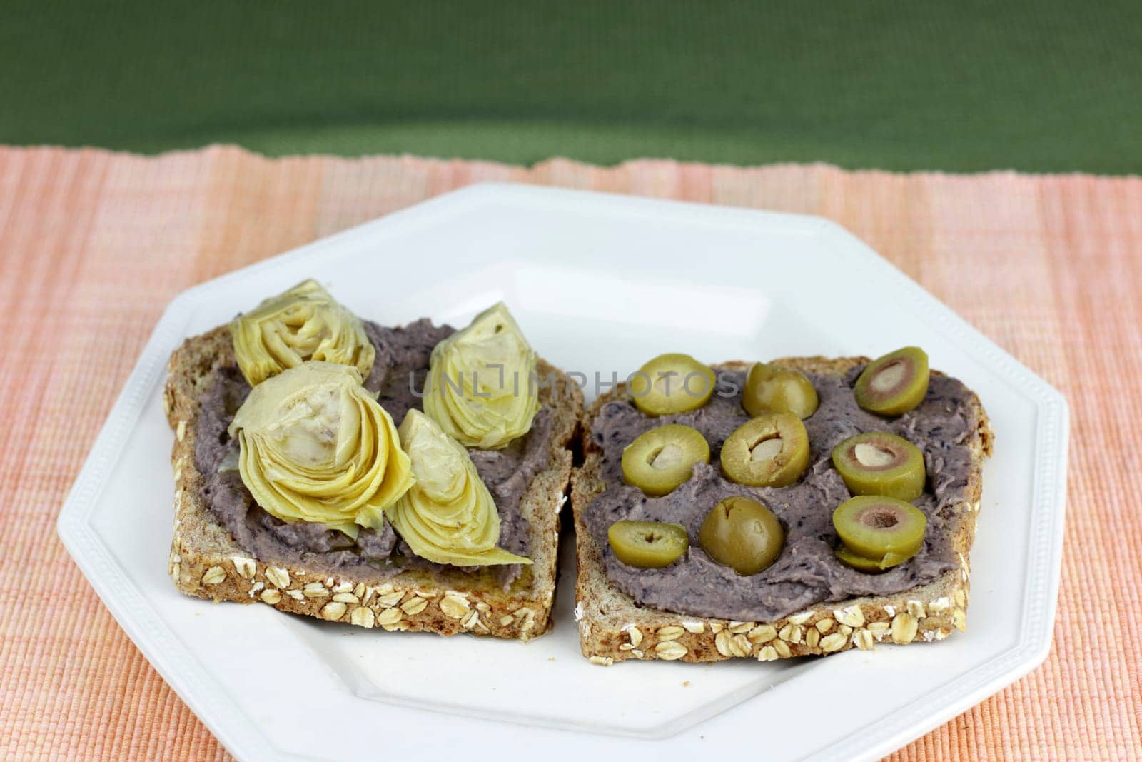 Food snack dinner of sprouted grain bread vegetarian bread with black bean hummus, artichoke hearts and garlic stuffed olives. Vegan meal of bread, black bean hummus, artichoke hearts, garlic olives