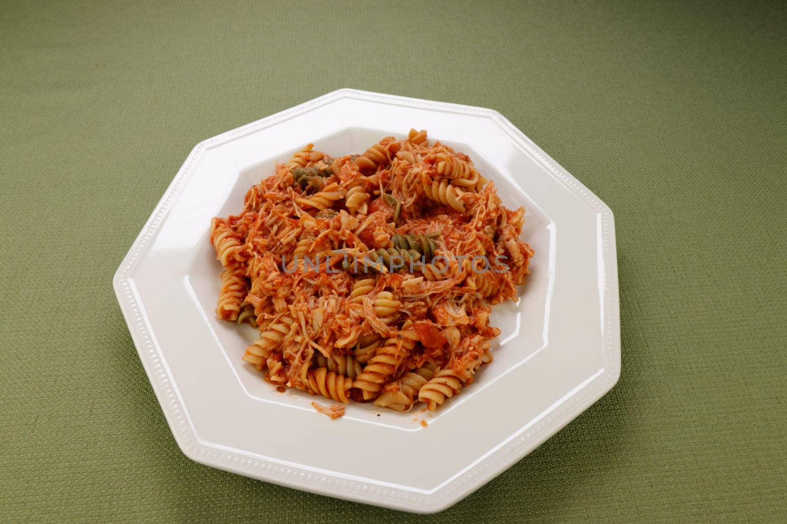 Spinach, carrot and tomato semolina and durum wheat tri-color rotini vegetable pasta with shredded chicken and tomato sauce on a plate. Vegetable rotini pasta mixed with chicken meat and tomato sauce.