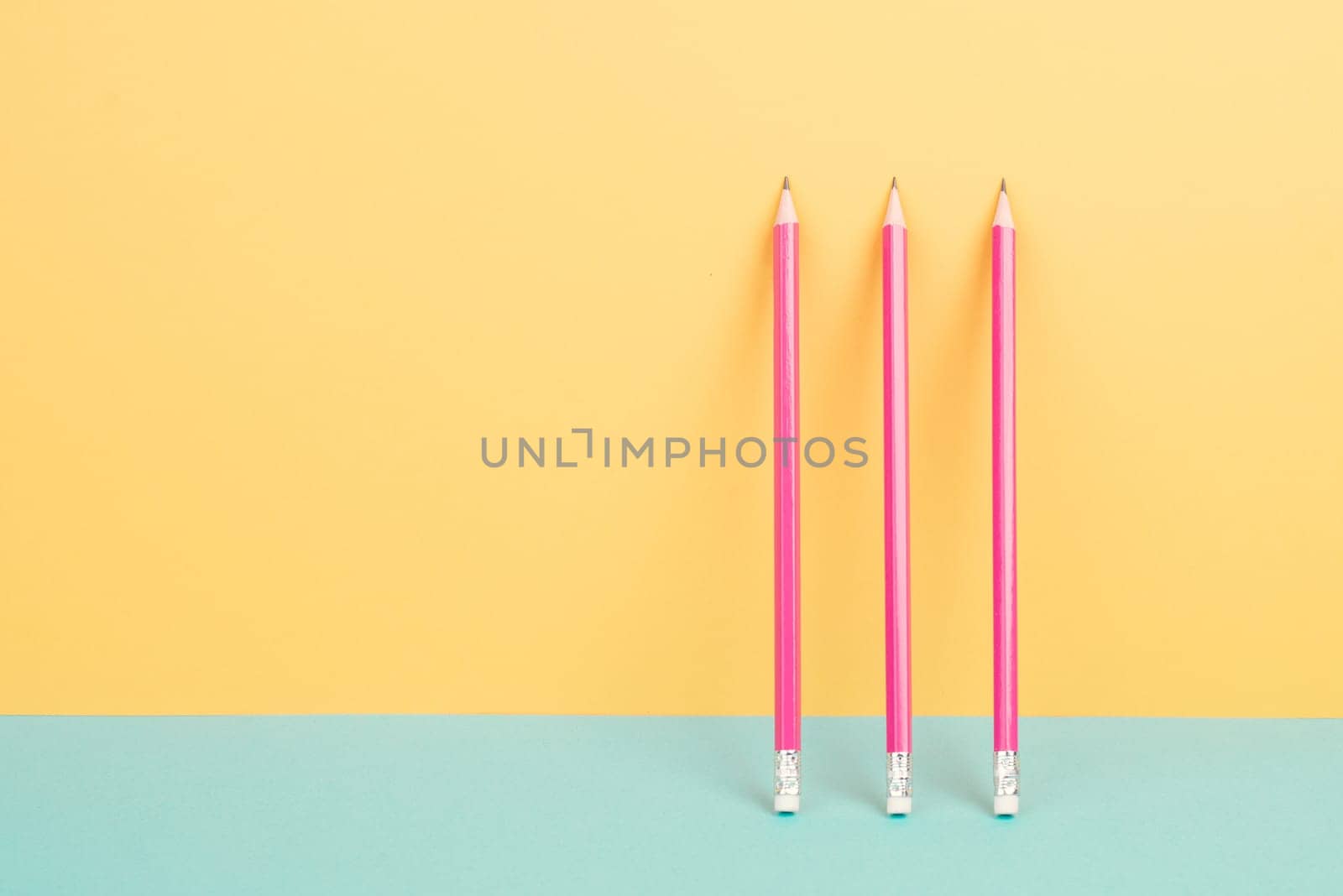 Pink pencils on a yellow and blue background, minimalism, creative, surreal and education concept, copy space for text, pastel colored wall