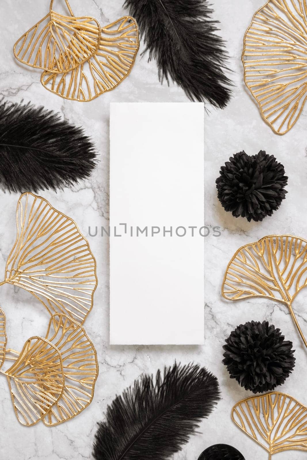 Blank card on marble table near black feathers and golden leaves with wedding rings top view. Menu or Invitation card mockup. Elegant femminine flat lay with vertical paper card