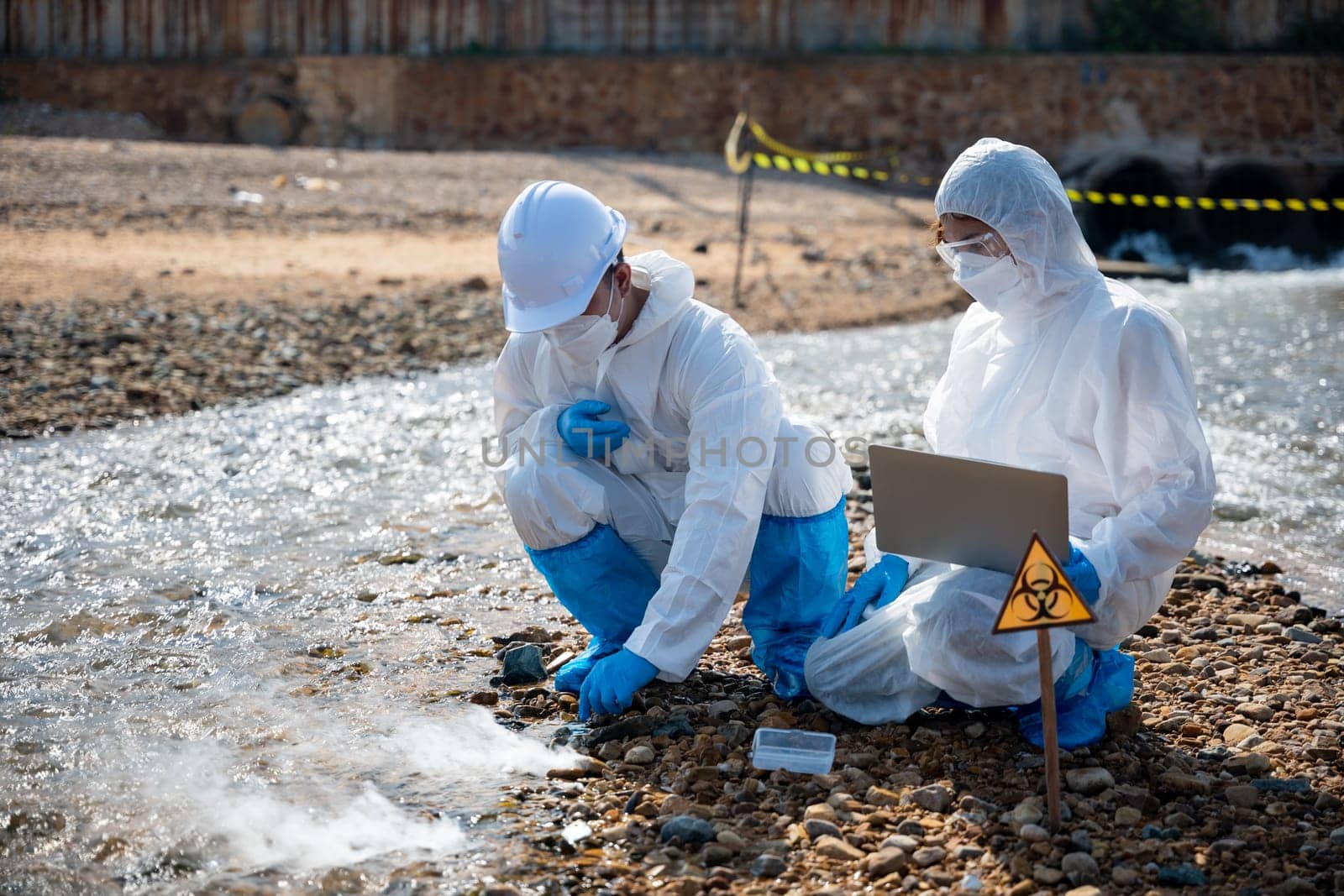 Biologist wear protective suit and mask collects sample of waste water from industry, problem environment, Ecologist sample taken dead fish to inspection and save data to laptop computer, Toxic water