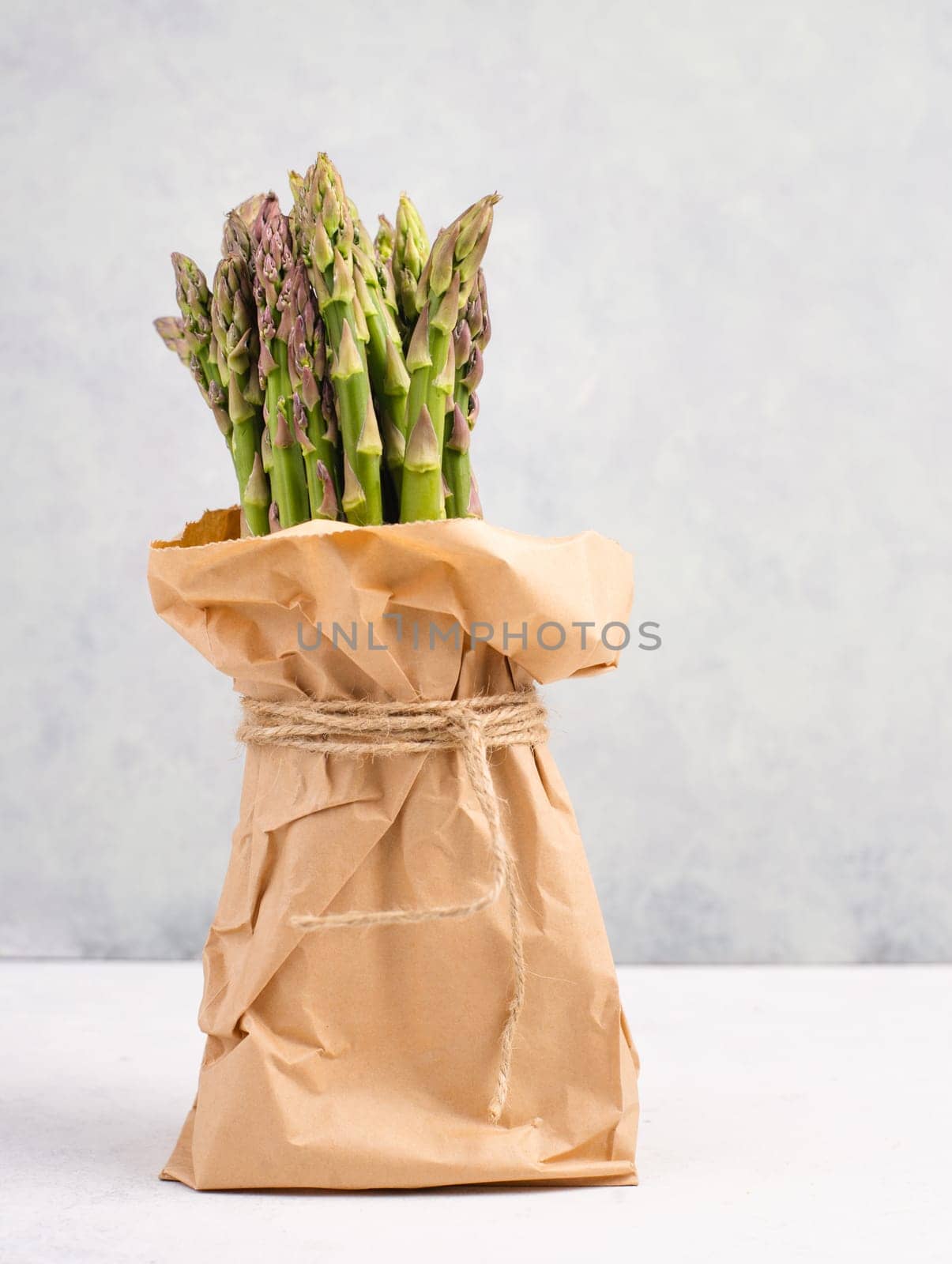 Fresh green bundle of asparagus on a white textured table, vegetables in spring, gourmet cuisine food, cooking a vegan meal