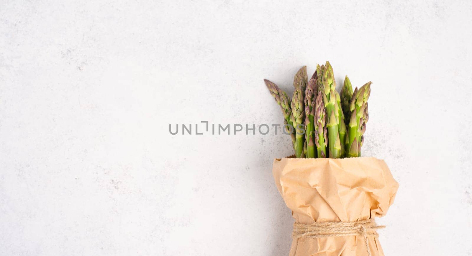 Fresh green bundle of asparagus on a white textured table, vegetables in spring, gourmet cuisine food, cooking a vegan meal
