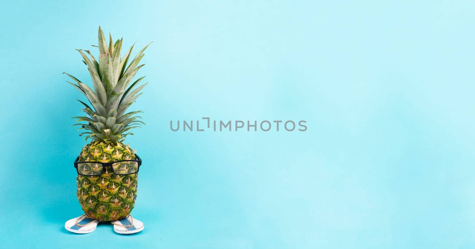 Pineapple with glasses and flip flops, vacation and travel concept, tropical summer holiday, funny fruit, blue background