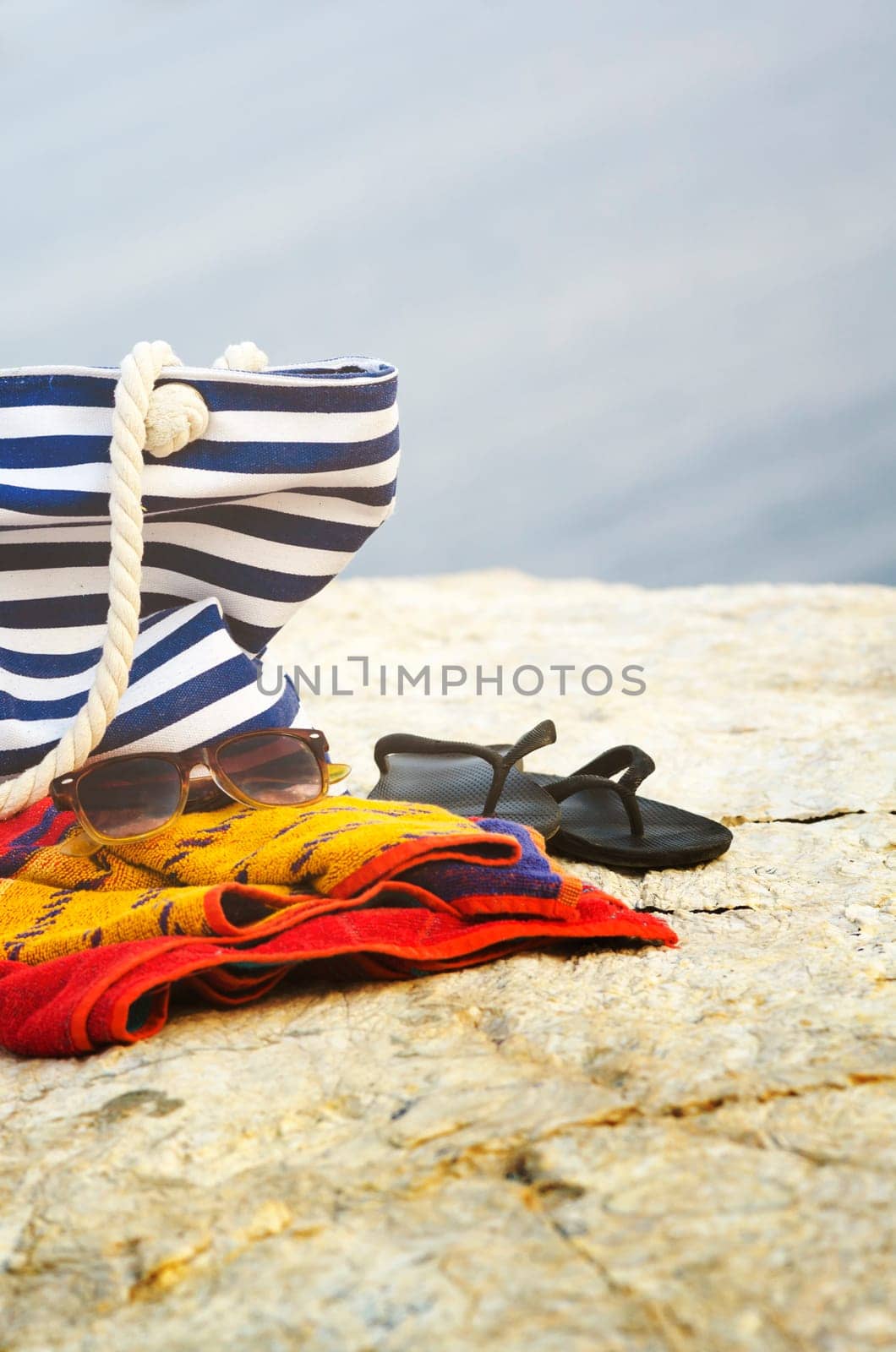 Sunglasses, towel, bag and flip-flops on the beach. Summer holiday concept.