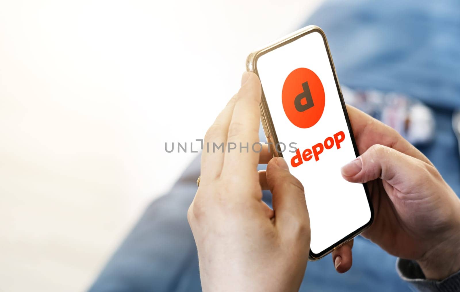 Rome, Italy, March 2022: Woman browsing Depop company website on her phone in her living room on a sunny day. Illustrative editorial. Realistic mockup. Selective focus.