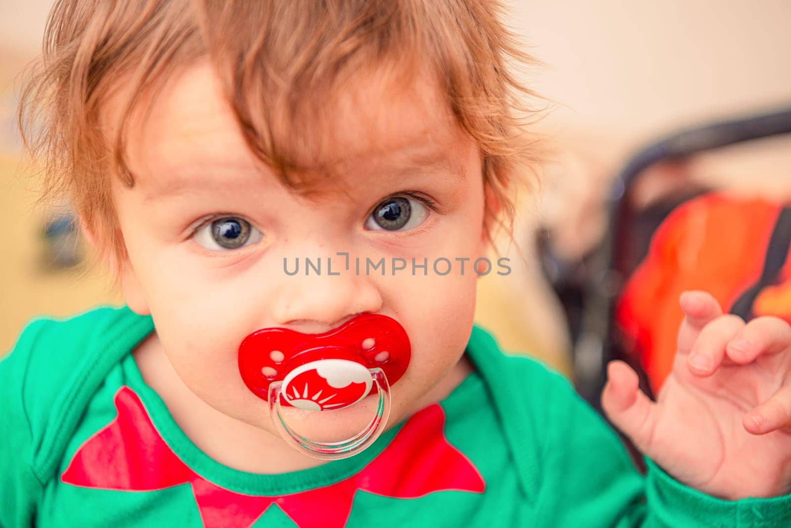 The face of a funny ginger baby with green eyes and red pacifier in his mouth