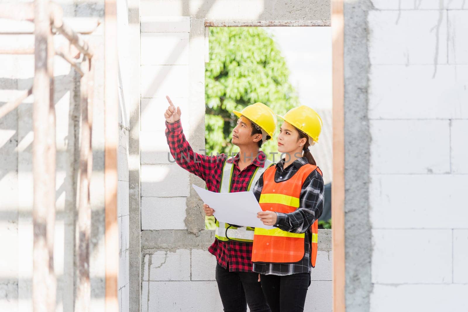 Architect and client discussing the plan with blueprint of the building at construction site. Asian engineer foreman worker man and woman working talking and checking on draw paper to checking project