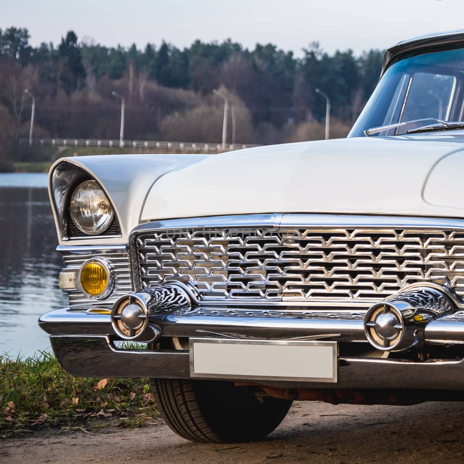 Old retro or vintage car or automobile front side with front lights or headlights and radiator grill on the lake