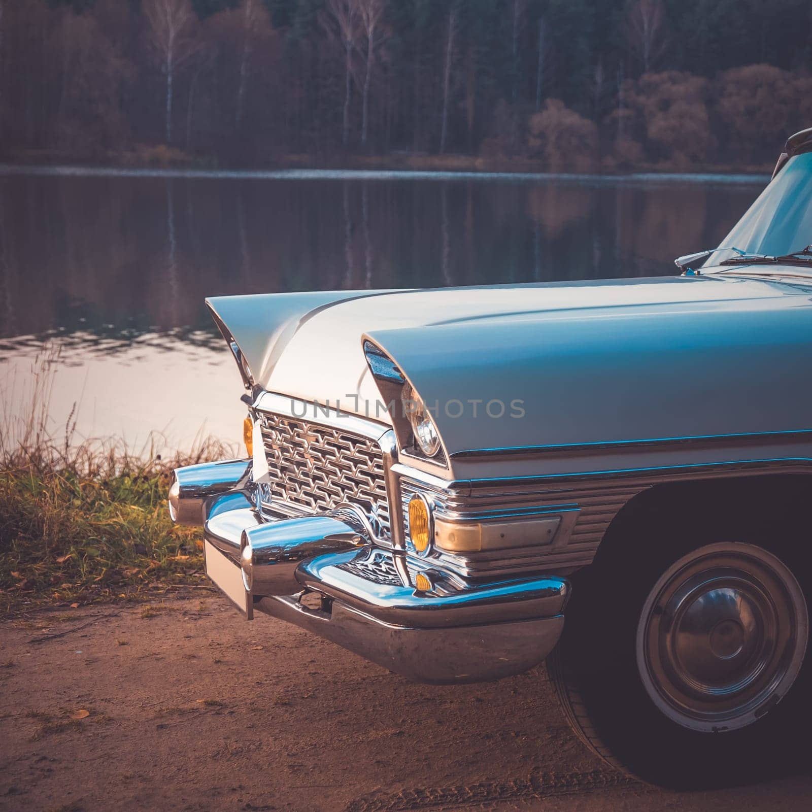 Old retro or vintage car or automobile front side with front lights or headlights and radiator grill on the lake. Processed by vintage or retro effect filter