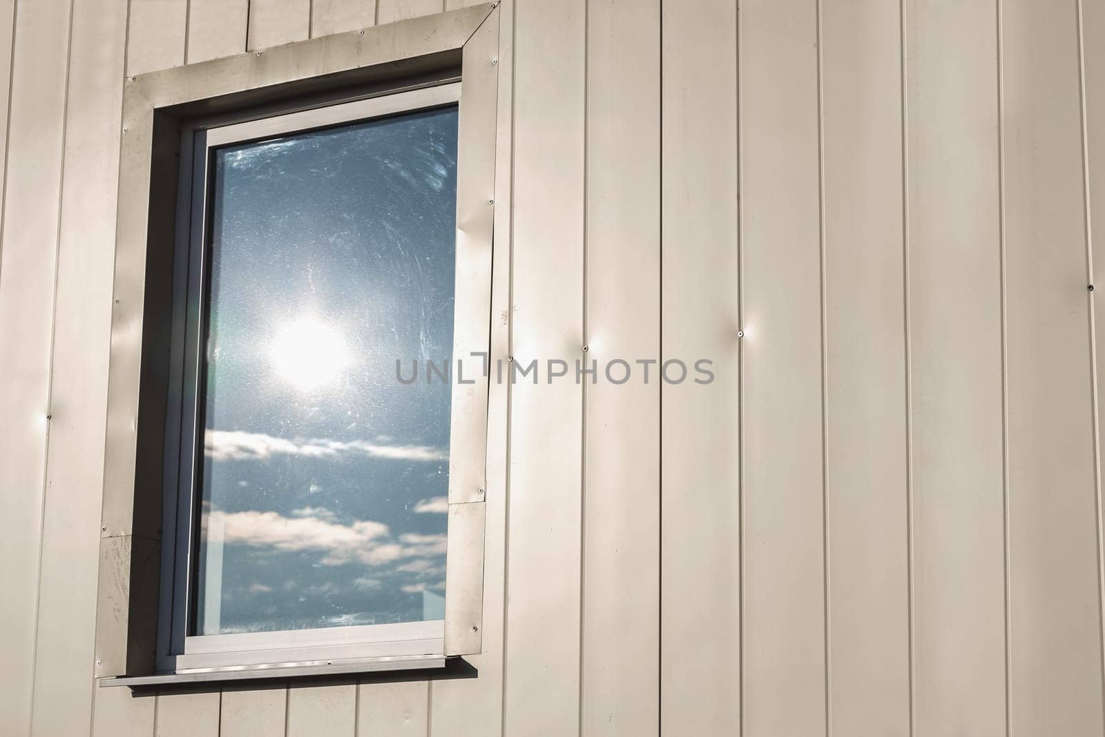 Window with sun reflection in light yellow color plastic siding panels wall