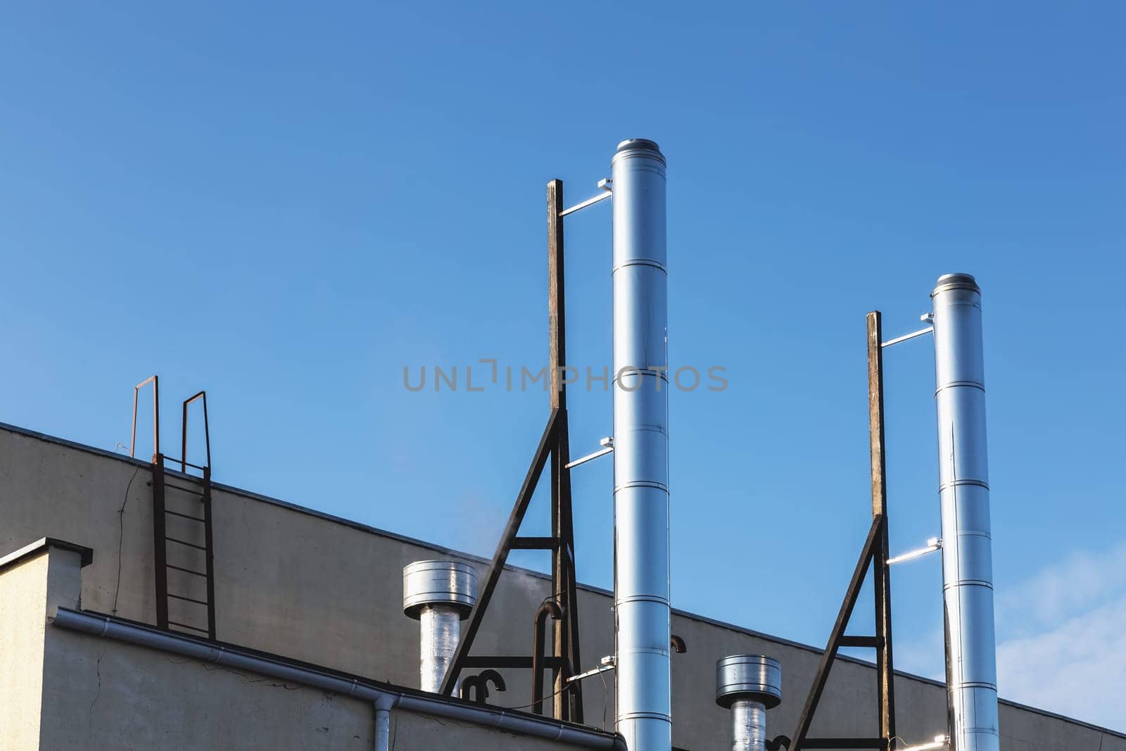 Smoke metal pipes on rooftop of industrial building against blue sky background