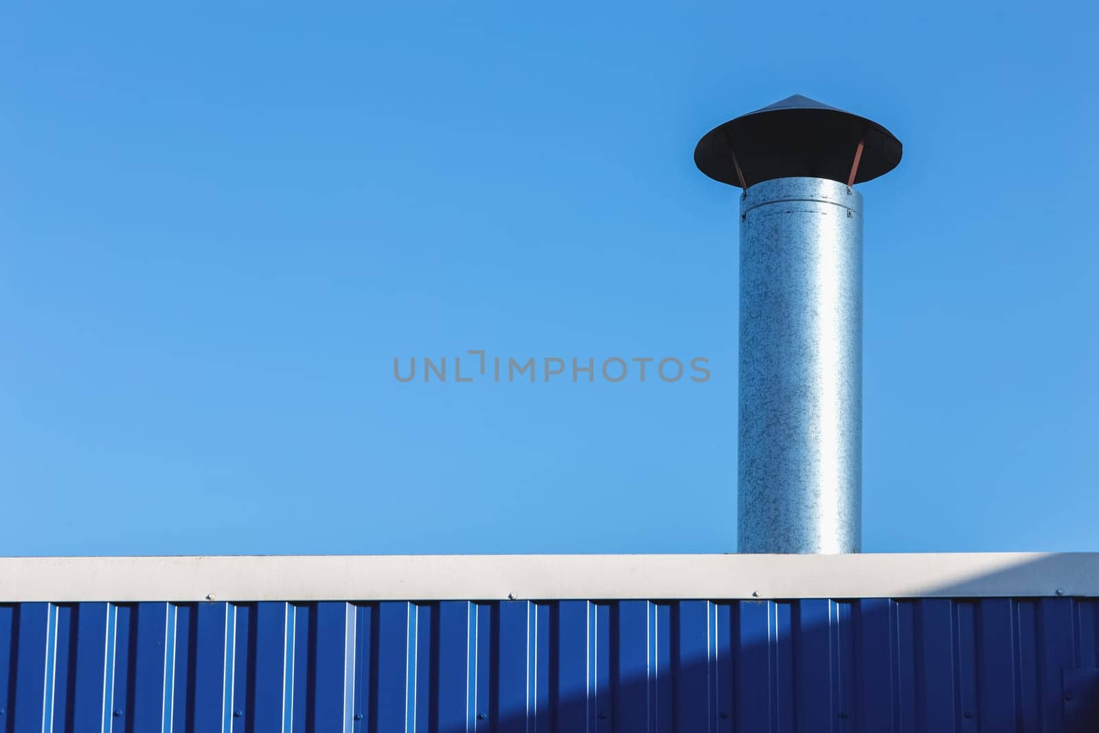 Metal chimney on building rooftop on blue sky background