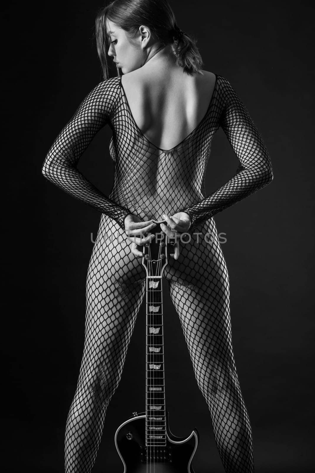 Sexy woman in fishnet body stocking holding an electric guitar.