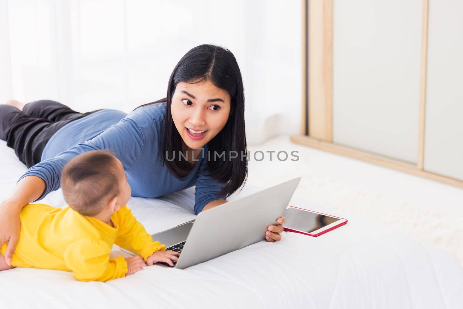 Asian new young beautiful mother finding and reads information on a laptop for milk mixing on a bottle in the bedroom at home