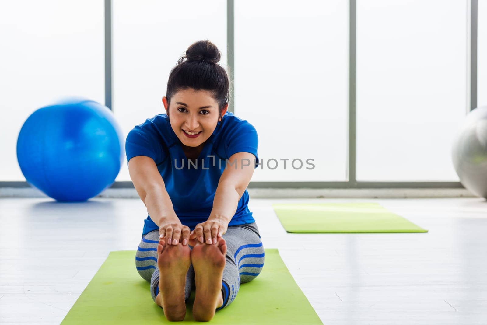Asian young woman wearing sportswear doing practicing yoga sitting stretching leg position indoor studio. female sport fit workout concept
