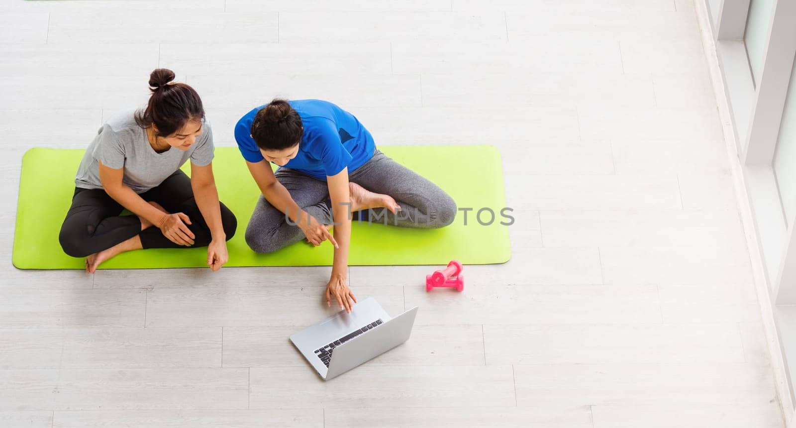 Overhead two Asian lifestyle adult and young woman in sportswear sitting floor on mat with dumbbells look laptop computer for training videos online in yoga studio, fit sport healthy workout exercise
