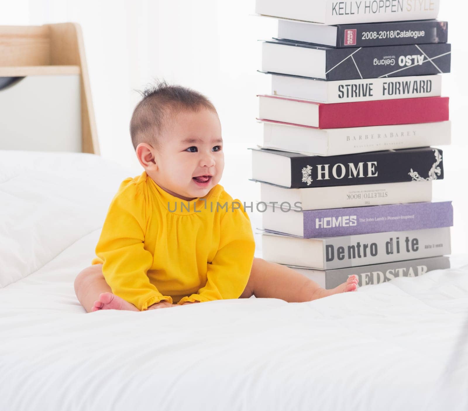 Asian cute baby little girl toddler looking at a stack of books on bedroom white bed, First baby library concept