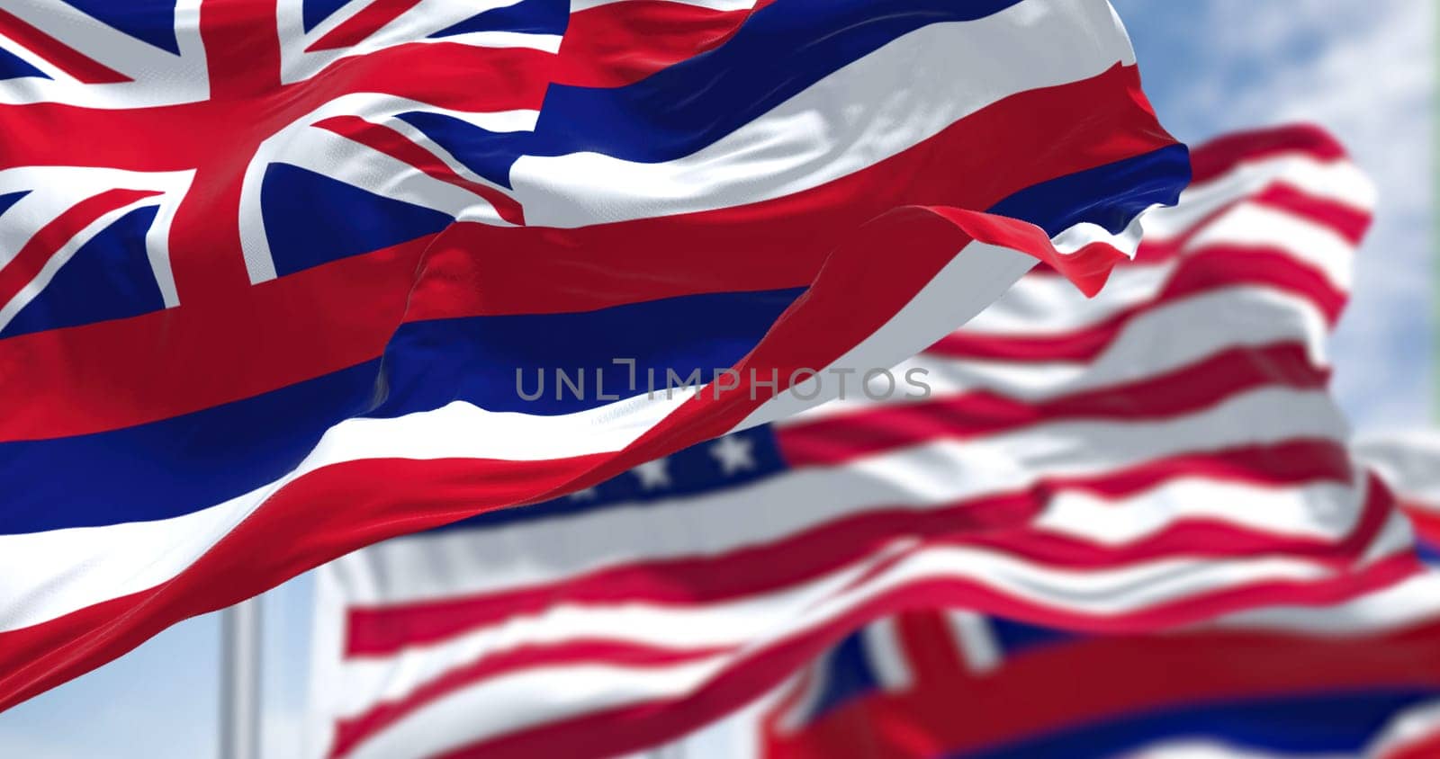 The Hawaii state flag waving along with the national flag of the United States of America. In the background there is a clear sky. Hawaii is a western state of the United States